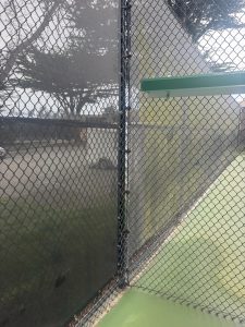 image shows two sides of a tennis court, one side the court and windscreen are clean, the other side the court and windscreen are dirty.